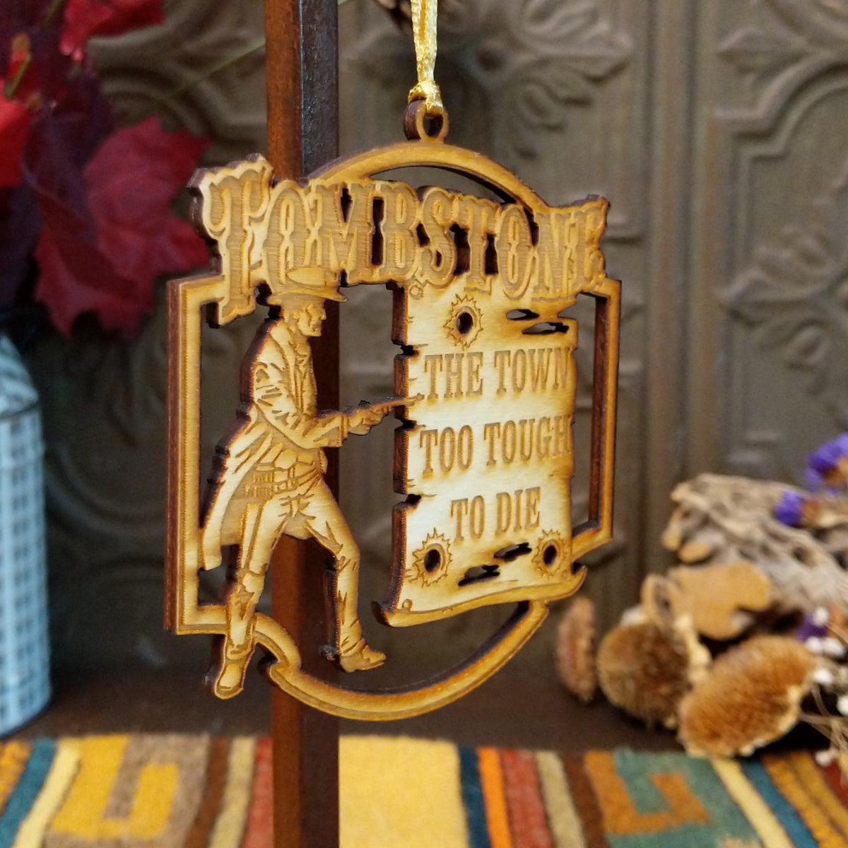 A laser-cut wooden hanging ornament featuring a cowboy silhouette and the words “The Town Too Tough to Die,” displayed against a rustic decorative background.