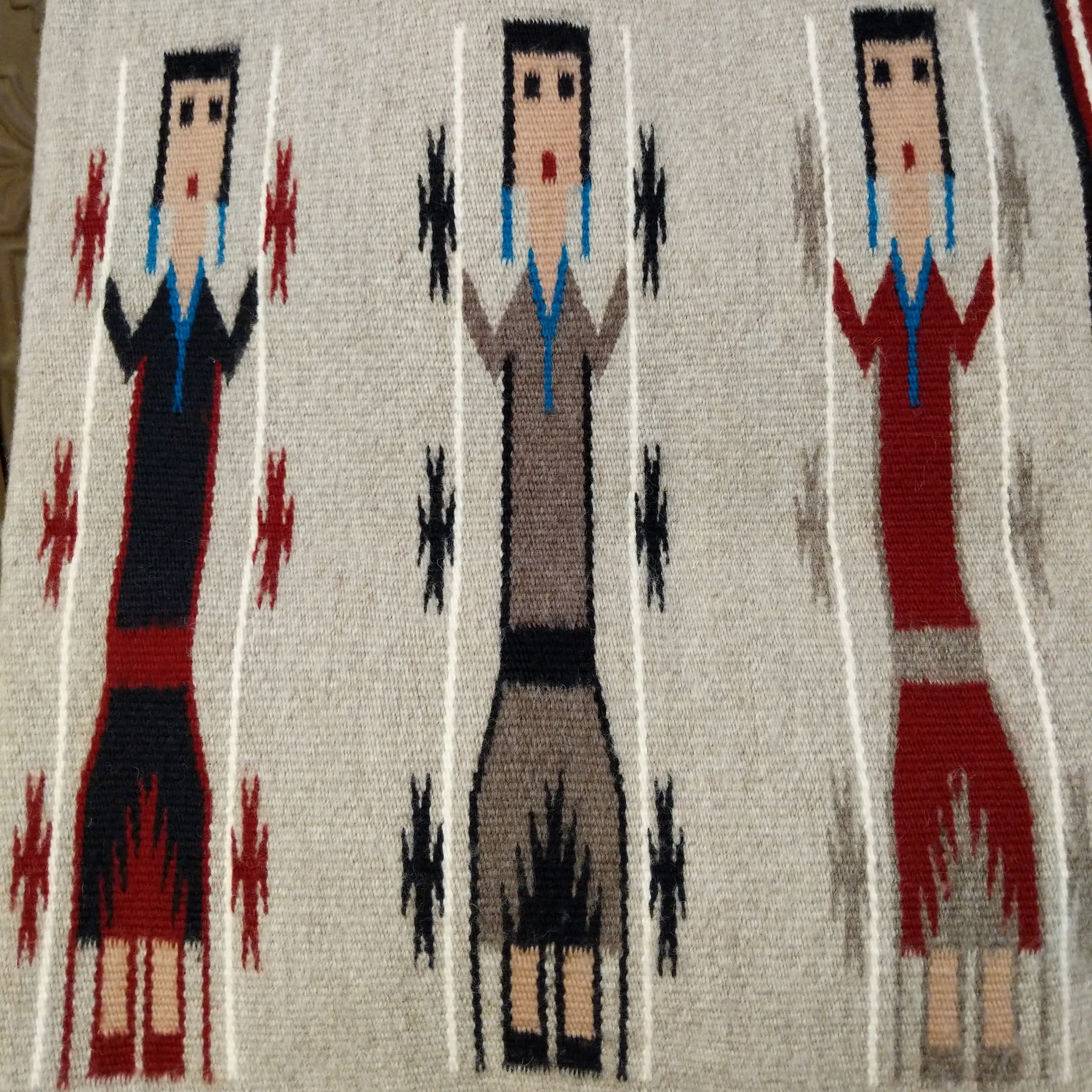 Yei Navajo rug by Milicent Platero featuring three traditional Yei figures on a natural gray background with geometric accents and a striped side border.