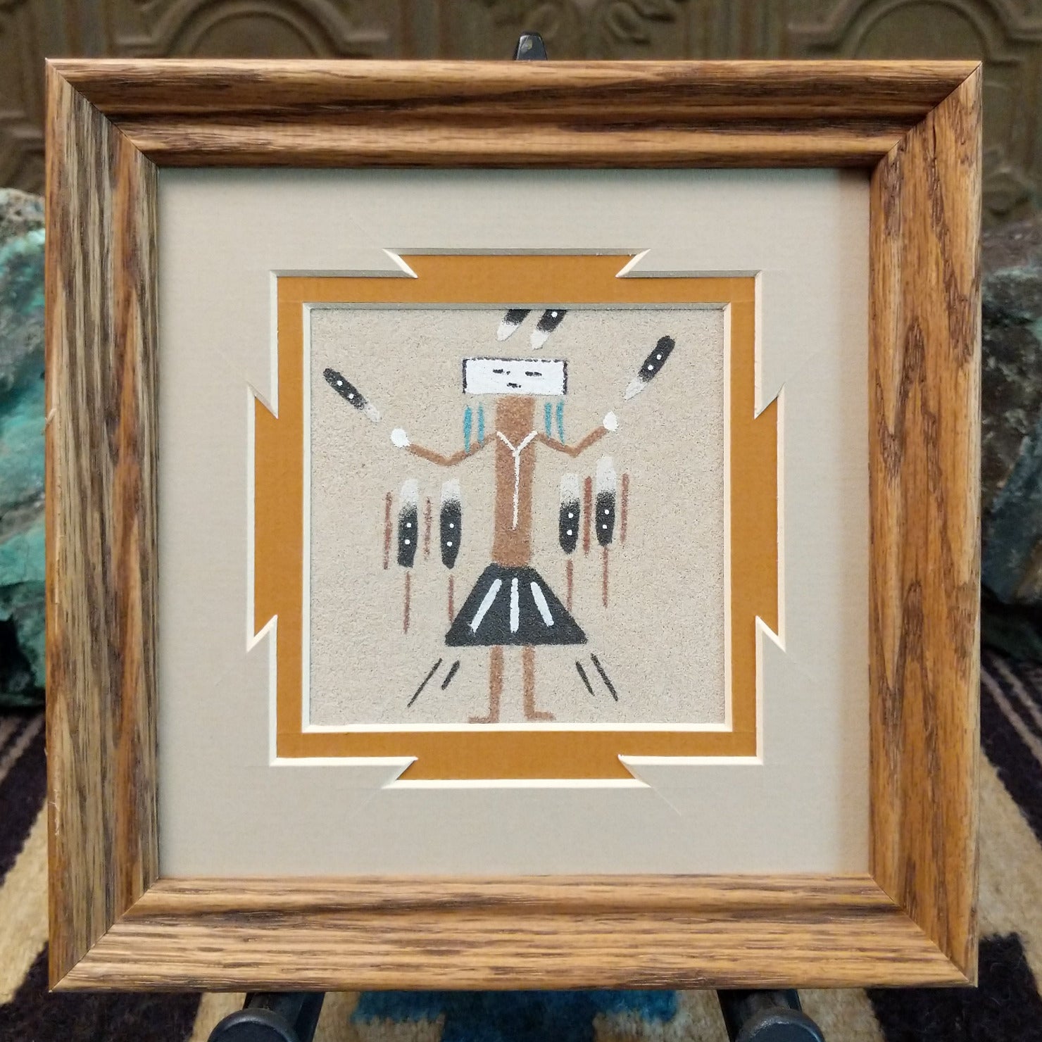 Framed Navajo sand painting of a Yei figure with raised arms.