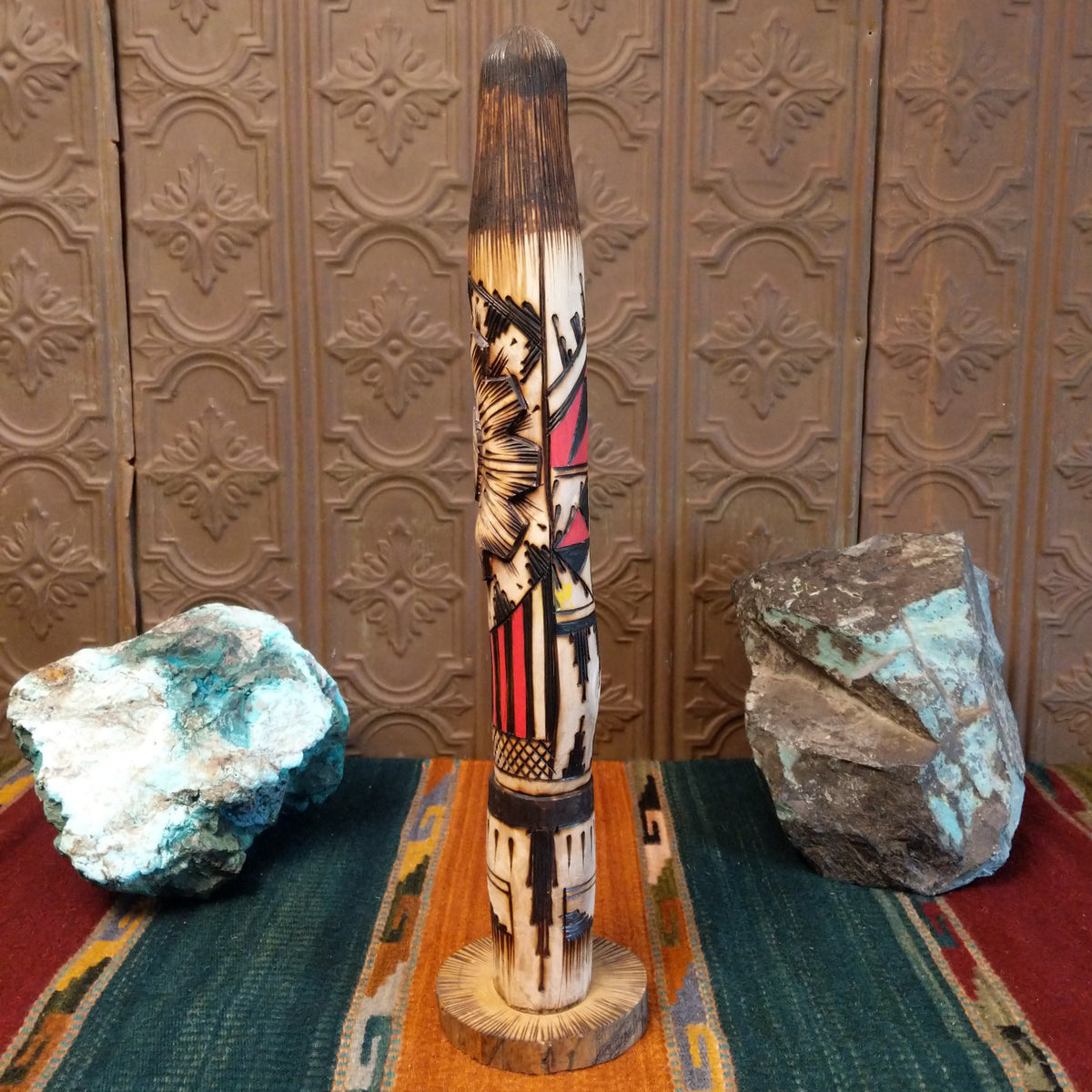This distinctive Yellowface Shalako Kachina by John Taylor features a tall, slender wooden carving with a yellow face, intricate black geometric patterns, colorful red and turquoise blue accents, and a round wooden display base.