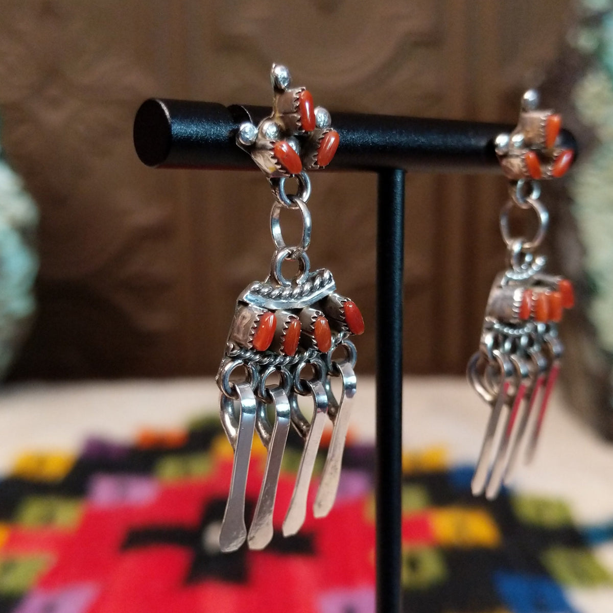 Zuni Coral Earrings featuring red-orange coral stones in detailed silver settings with clustered accents and multiple long dangling silver elements; side view.