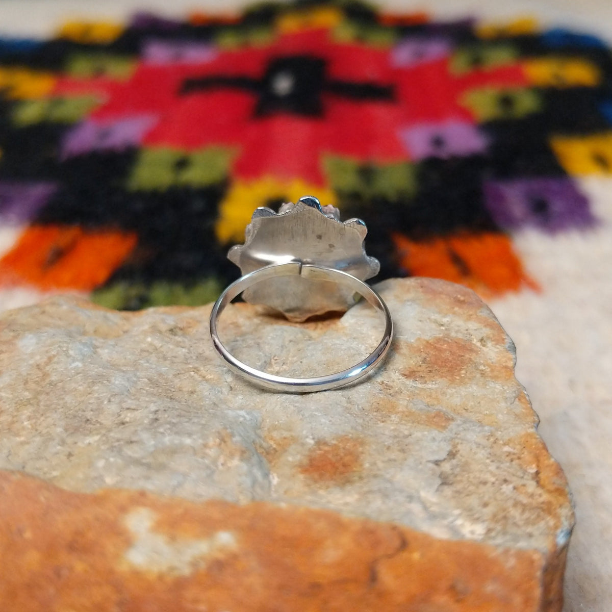 This vibrant Zuni Coral Flower Ring features teardrop-shaped red coral stones arranged as flower petals around a raised silver center, accented with rounded silver details; underside view.