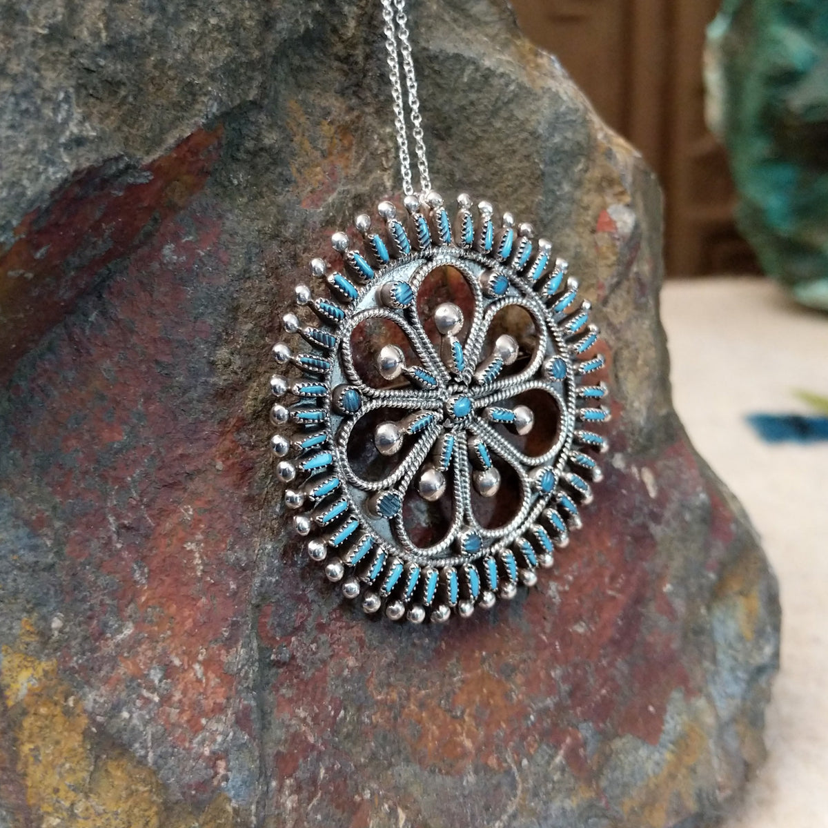 Zuni needlepoint turquoise pendant and pin by Vincent Johnson featuring slender turquoise stones arranged around a circular silver frame with intricate twisted-wire floral details and silver accents; side view.