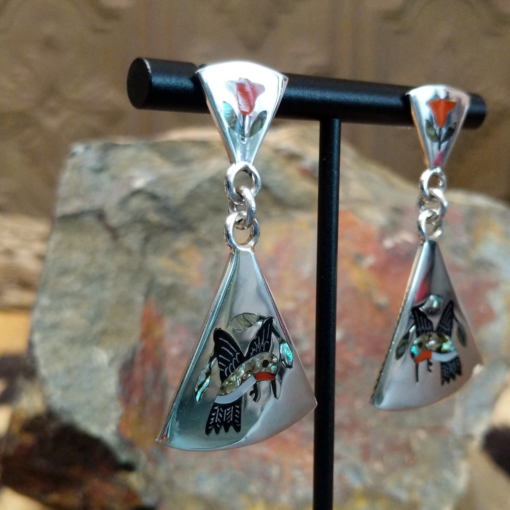 Handcrafted sterling silver Zuni hummingbird inlay earrings by Sanford Edaakie, featuring a two-piece dangle design with colorful flowers and hummingbirds; side view.