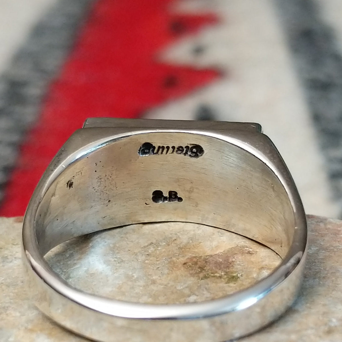 Zuni inlay ring by S.B. featuring a rectangular geometric design in turquoise, black onyx, coral, and mother of pearl inlay set in a polished silver band; artisan and Sterling Silver stamp.