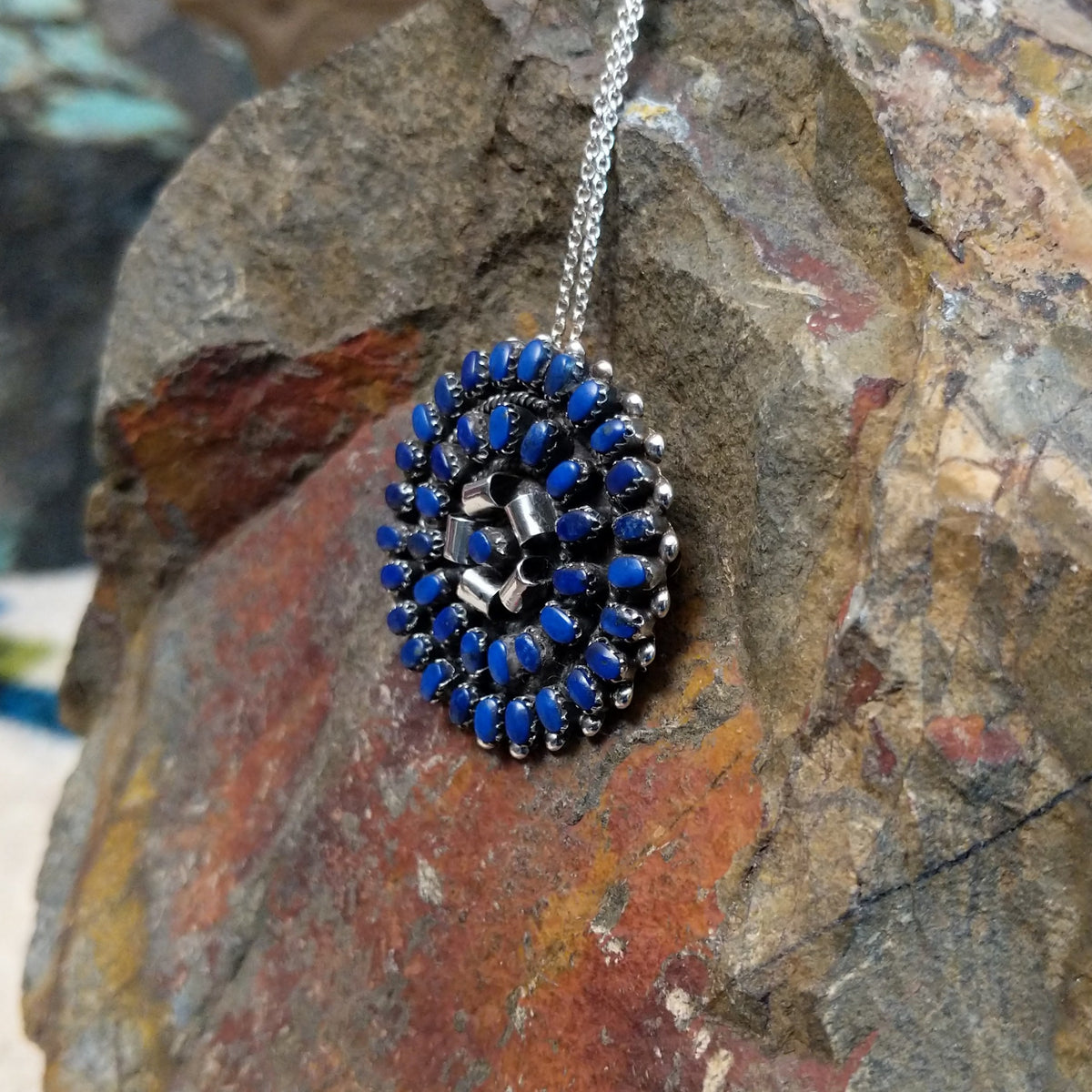 Zuni lapis cluster pendant and pin by Lorraine Waatsa featuring deep blue lapis stones arranged in concentric circles with twisted and sculptural silver detailing; side view.