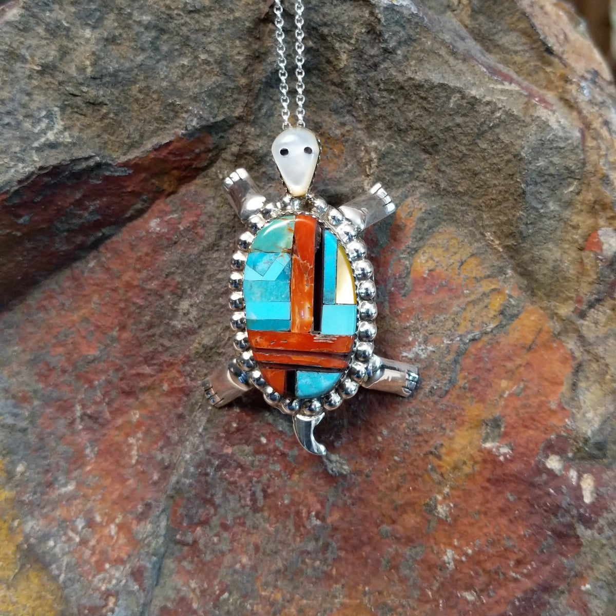 Zuni multistone turtle pendant and pin by W.J.H. featuring colorful turquoise, red-orange, black, and cream inlay set in a detailed silver turtle design.