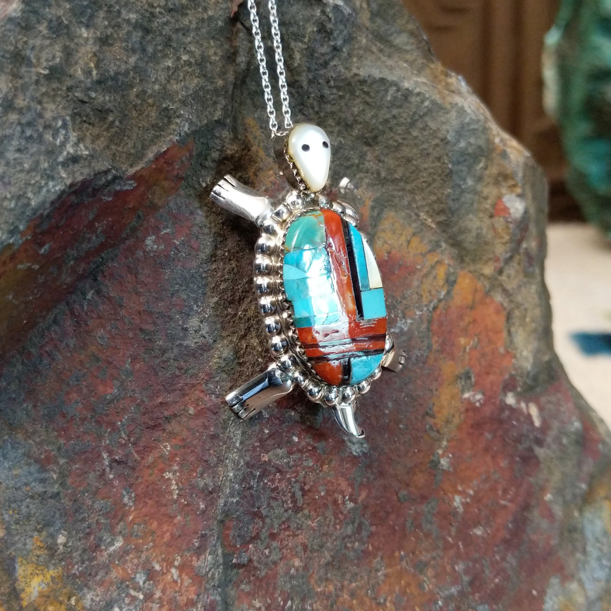 Zuni multistone turtle pendant and pin by W.J.H. featuring colorful turquoise, red-orange, black, and cream inlay set in a detailed silver turtle design; side view.