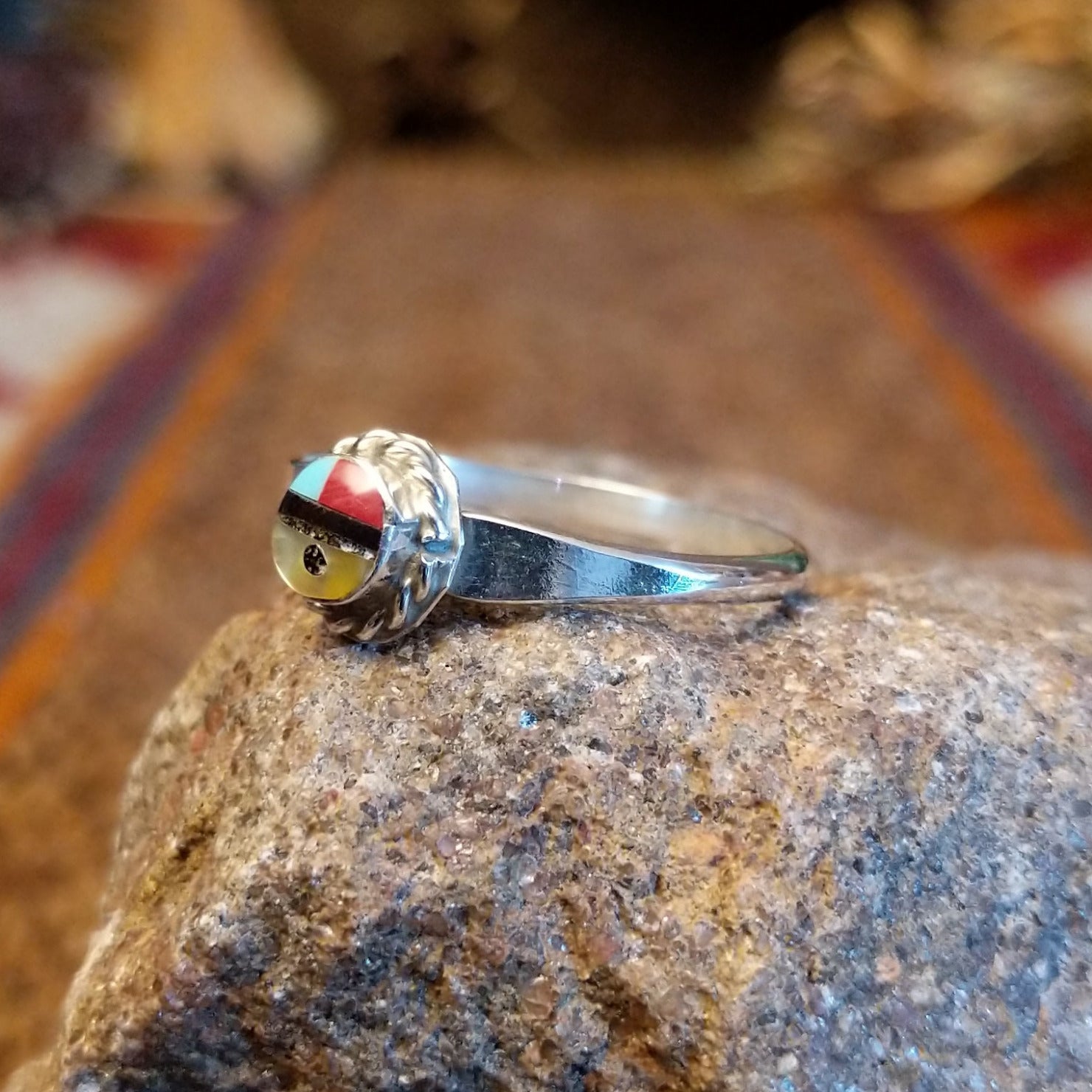 Sterling silver ring with sunface design crafted with turquoise, mother of pearl, black onyx, and coral that is framed by twisted rope detailing.