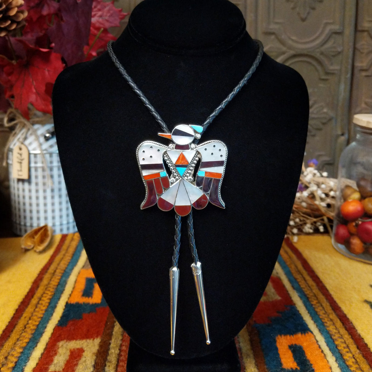 Zuni Thunderbird Bolo Tie by Bobby Shack featuring a detailed silver thunderbird with colorful turquoise, coral red, white, and black geometric inlay, outstretched wings, braided black leather cord, and polished silver tips.