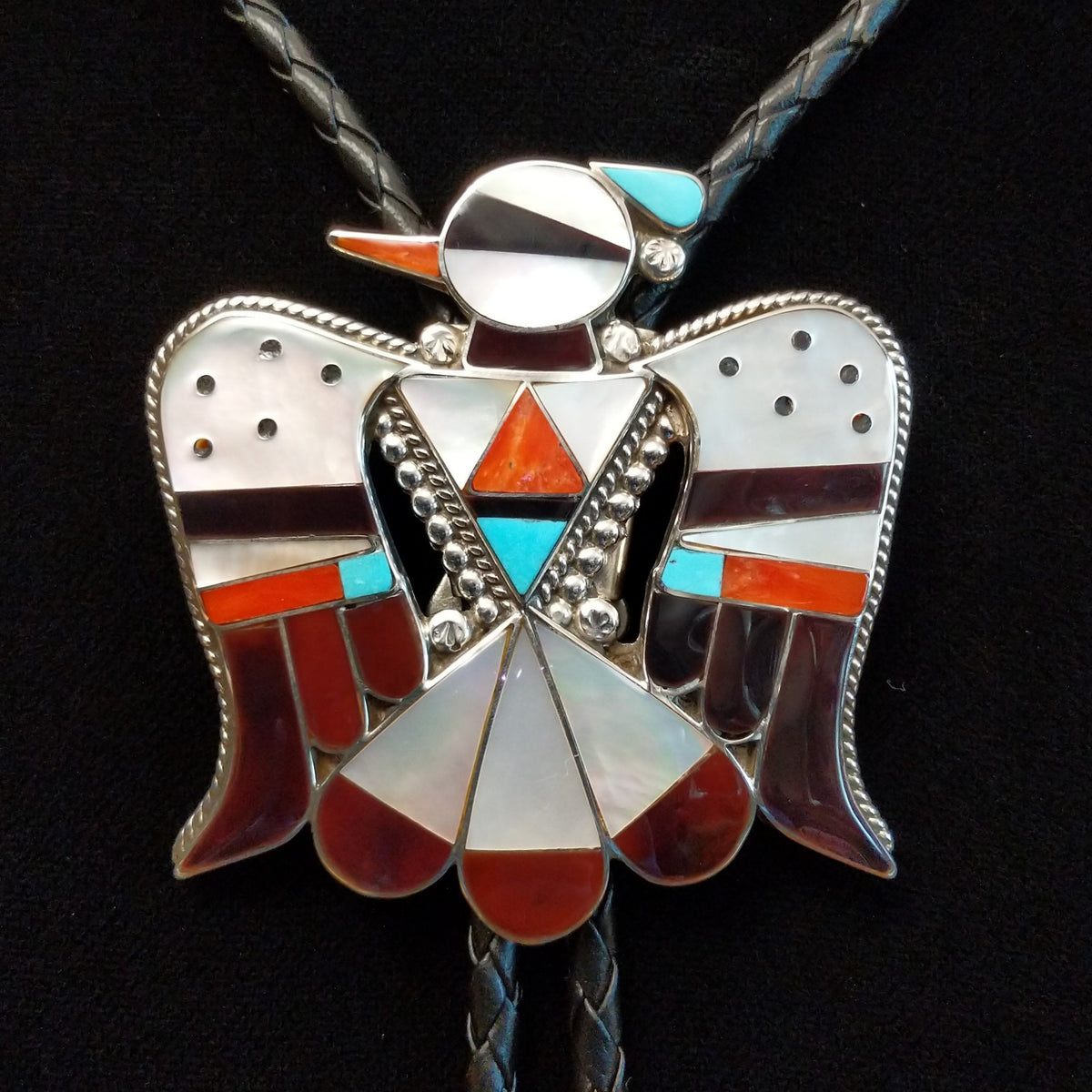 Zuni Thunderbird Bolo Tie by Bobby Shack featuring a detailed silver thunderbird with colorful turquoise, coral red, white, and black geometric inlay, outstretched wings, braided black leather cord, and polished silver tips.