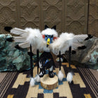 Navajo-made eagle kachina doll by M. C. with white feathered wings, blue mask, yellow beak, and black garments.