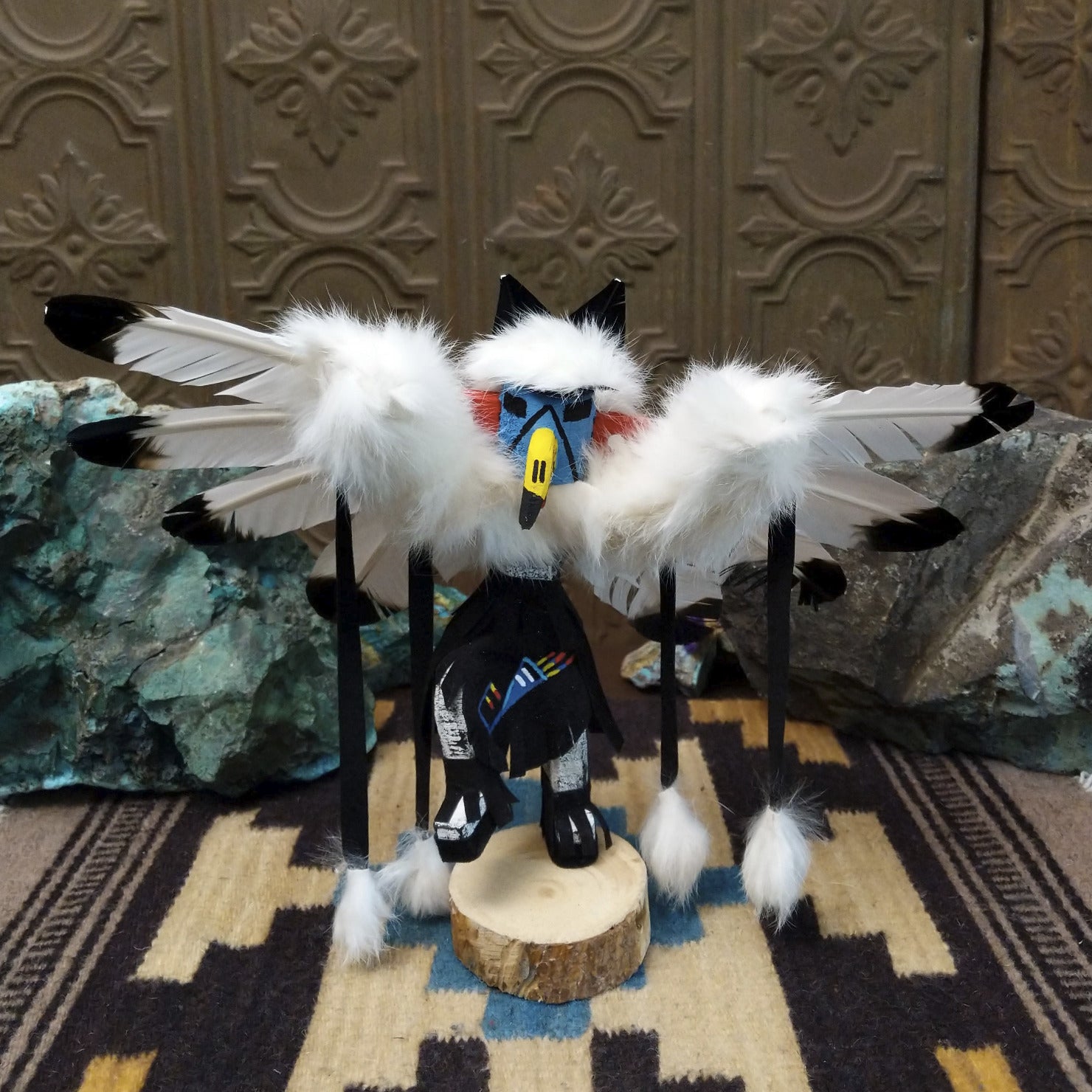 Navajo-made eagle kachina doll by M. C. with white feathered wings, blue mask, yellow beak, and black garments.