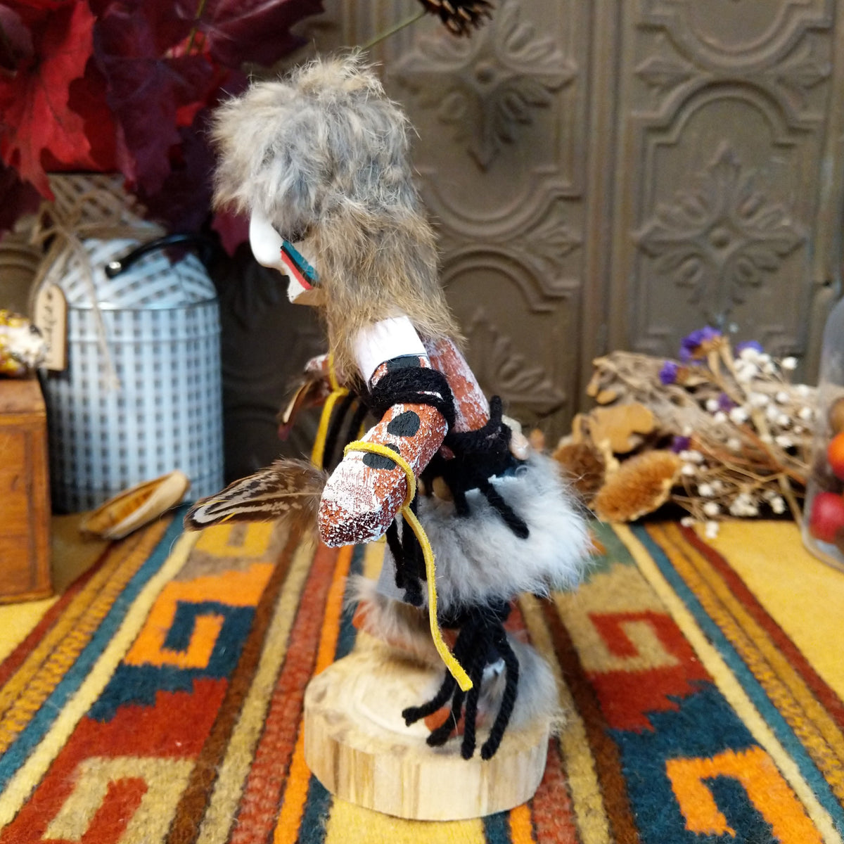 Side view of the Navajo Field House Kachina doll with gray fur headdress, white painted face, red and turquoise cheek markings, and light blue fabric apron.