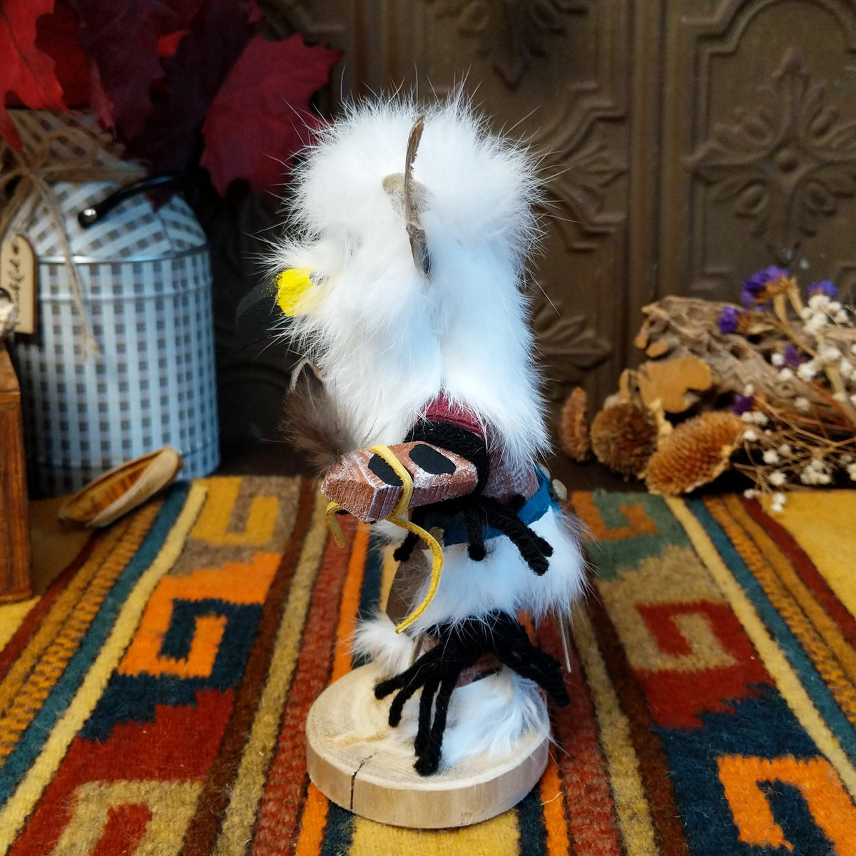 Side view of the Navajo Owl Kachina doll with fluffy white fur, black eyes, yellow-trimmed beak, brown feathers around the head, and blue belt.