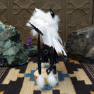 Navajo-made eagle kachina doll by M. C. with white feathered wings, blue mask, yellow beak, and black garments.