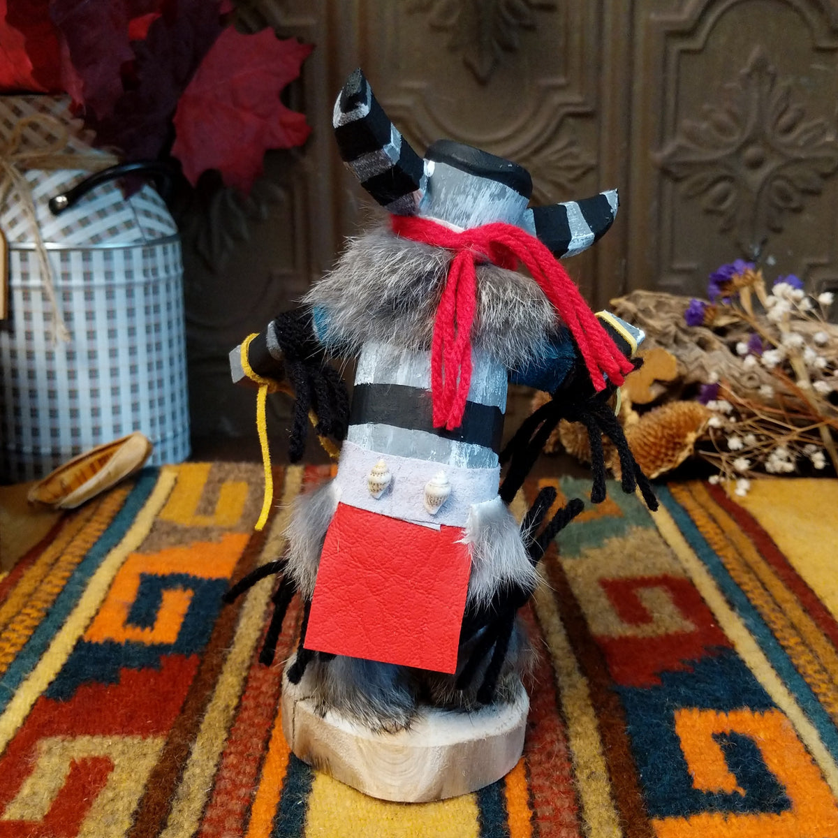 Back view of the Navajo Clown Kachina doll with black-and-silver striped horns, smiling painted face, gray fur, striped body, and red fabric apron.