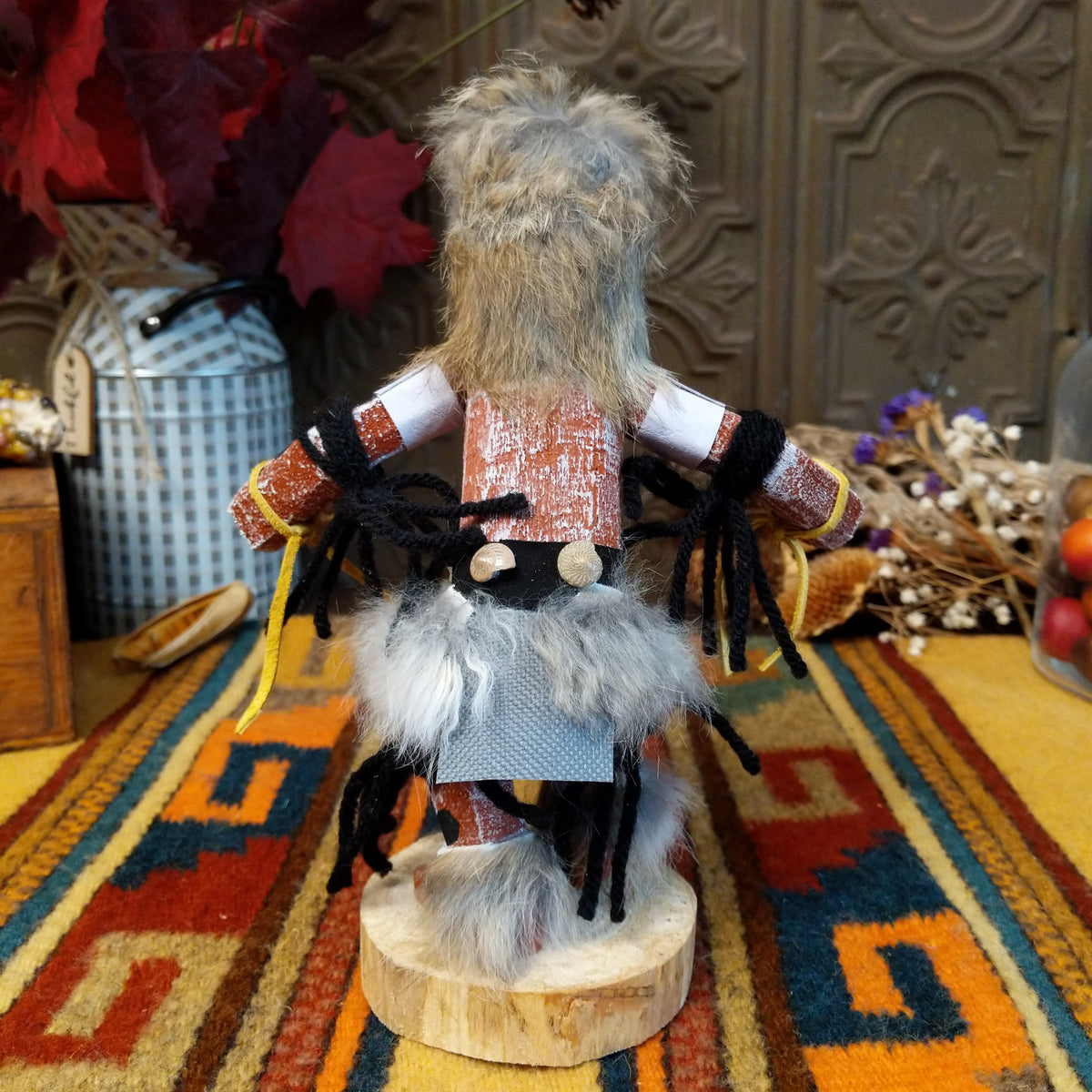 Back view of the Navajo Field House Kachina doll with gray fur headdress, white painted face, red and turquoise cheek markings, and light blue fabric apron.