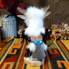 Back view of the Navajo Owl Kachina doll with fluffy white fur, black eyes, yellow-trimmed beak, brown feathers around the head, and blue belt.