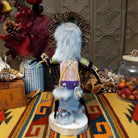 Back view of the Navajo Sunface Kachina doll with turquoise-colored face, feather headdress, outstretched arms, and blue fabric clothing.