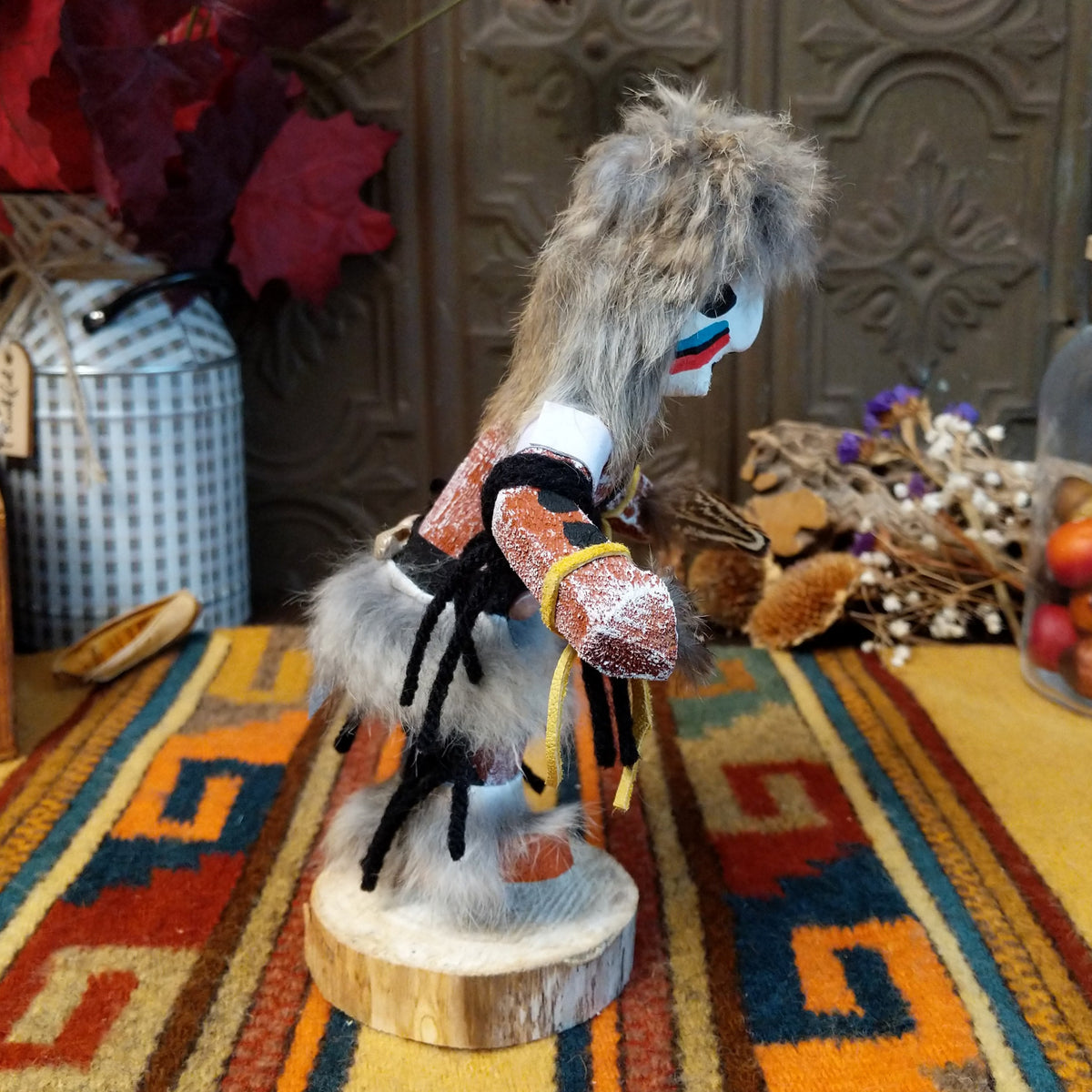 Side view of the Navajo Field House Kachina doll with gray fur headdress, white painted face, red and turquoise cheek markings, and light blue fabric apron.