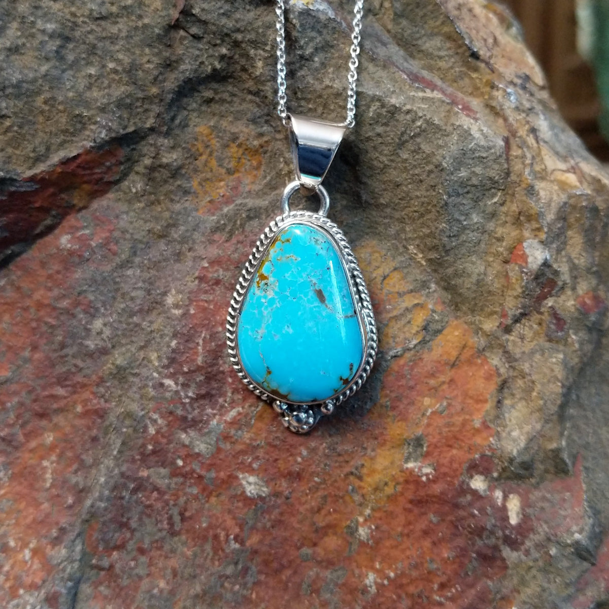 #8 turquoise pendant by Burt Francisco featuring a large teardrop-shaped blue turquoise stone with brown and golden matrix framed in twisted sterling silver.