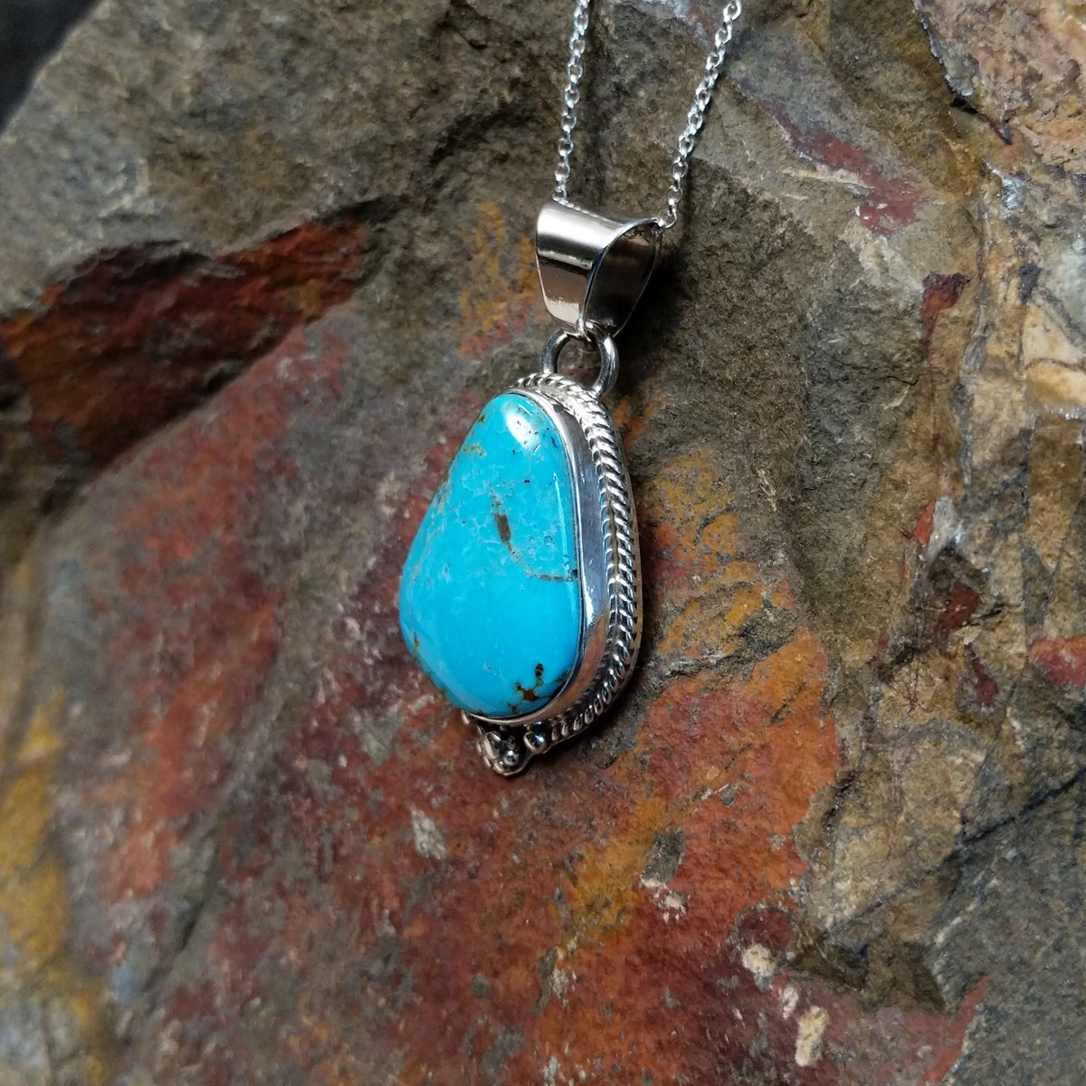 #8 turquoise pendant by Burt Francisco featuring a large teardrop-shaped blue turquoise stone with brown and golden matrix framed in twisted sterling silver; side view.