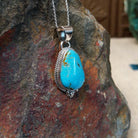 #8 turquoise pendant by Burt Francisco featuring a large teardrop-shaped blue turquoise stone with brown and golden matrix framed in twisted sterling silver; side view.