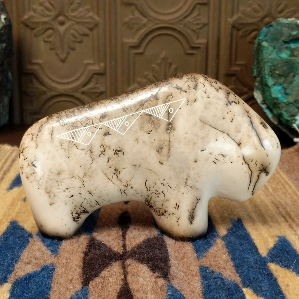 White clay molded into a bison figure with fired horsehair along its body and unique etched patterns on its body.