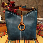 Alexa Handbag by Liz Soto featuring a tall structured silhouette, decorative contrast stitching, vertical center detailing, large wrapped circular accent, and wide shoulder strap.