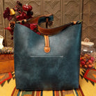 Alexa Handbag by Liz Soto featuring a tall structured silhouette, decorative contrast stitching, vertical center detailing, large wrapped circular accent, and wide shoulder strap; back.