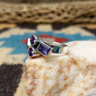 Amethyst ring by Ann Curley, featuring four faceted purple amethyst gemstones in round, square, rectangular, and pear shapes set in a handcrafted sterling silver ring.  Side view.