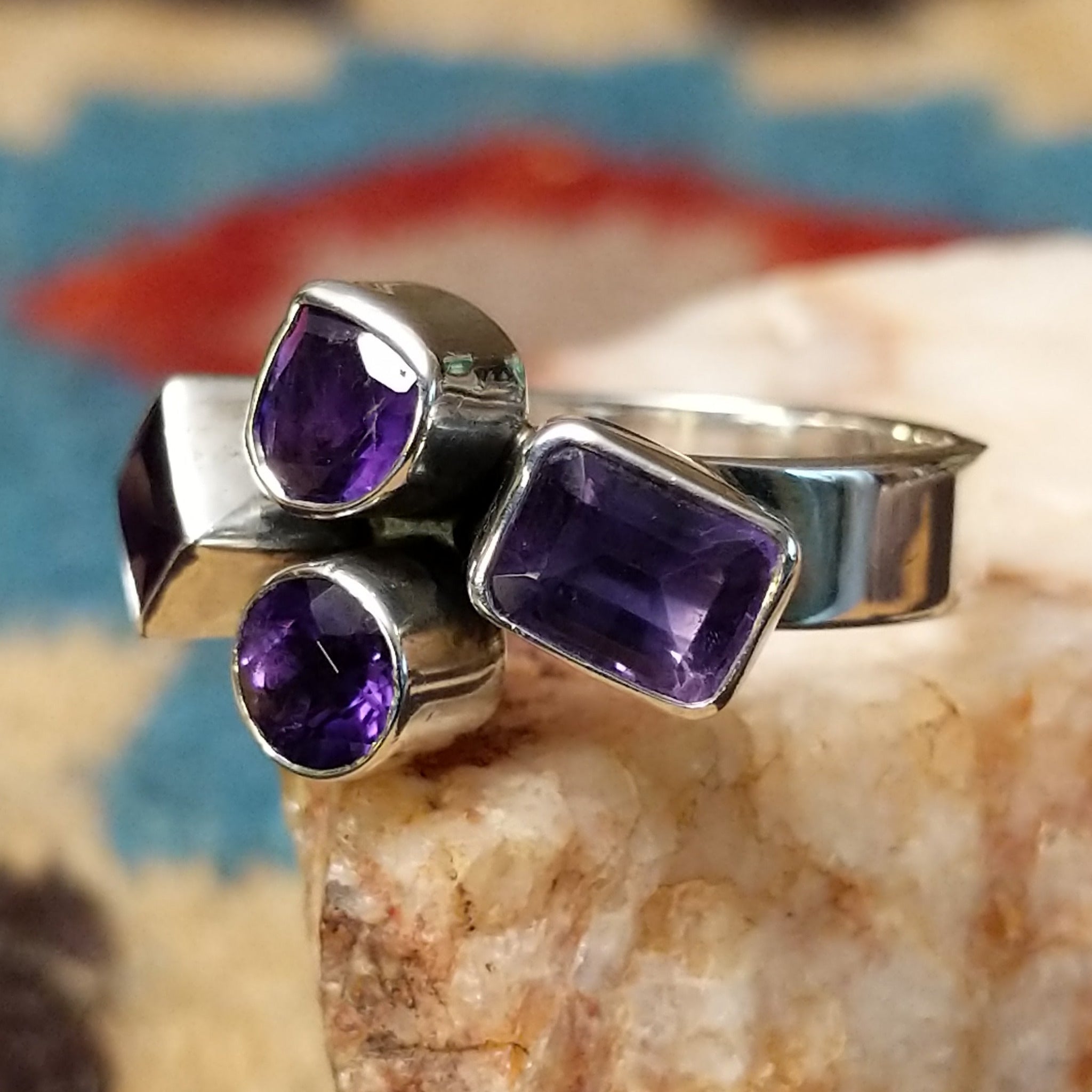 Amethyst ring by Ann Curley, featuring four faceted purple amethyst gemstones in round, square, rectangular, and pear shapes set in a handcrafted sterling silver ring.  Side view.