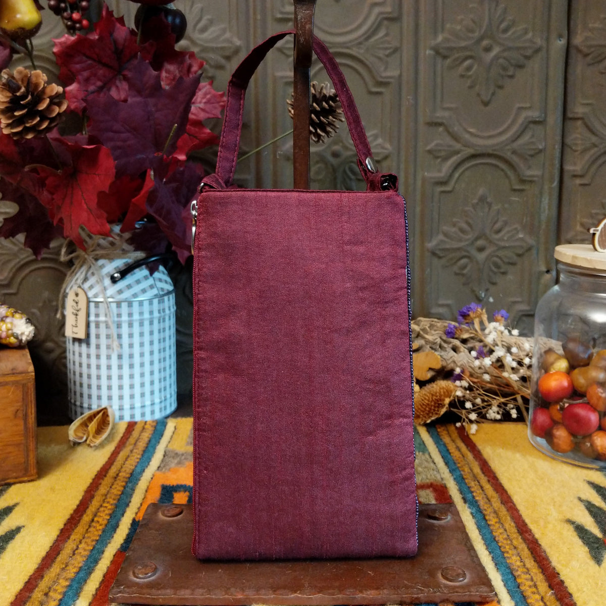 Aztec Club Bag by Bamboo Trading featuring intricate turquoise, pink, plum, and purple geometric patterns with diamond motifs, embroidered details, shimmering beadwork, sequins, and a coordinating burgundy shoulder strap; back side view.