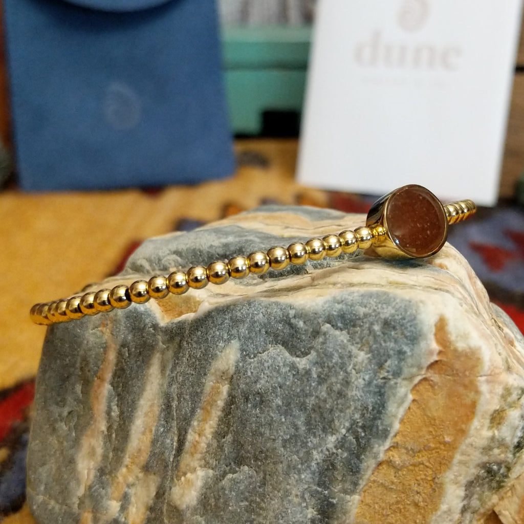 Beaded cuff bracelet with a gold-plated brass frame, featuring an oval sand-filled center.