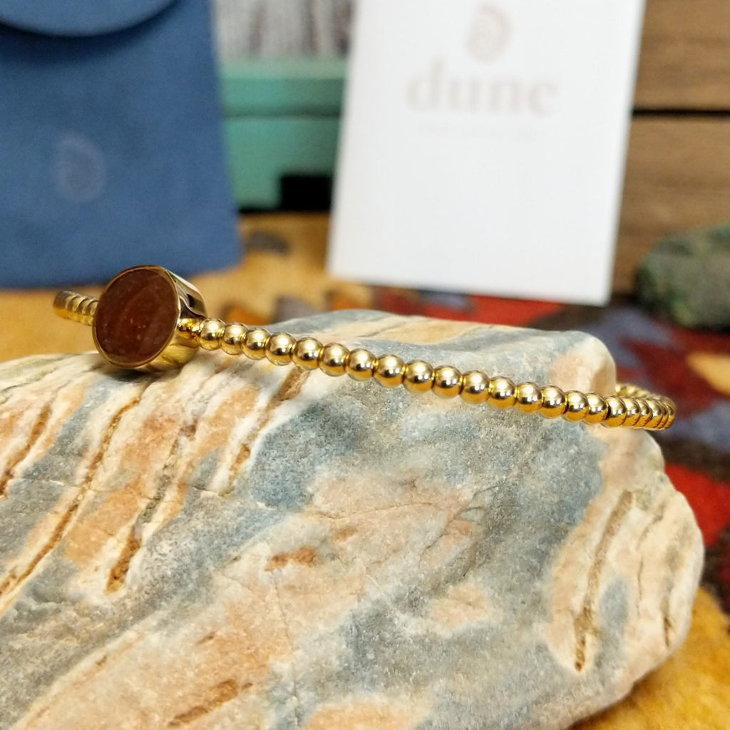 Beaded cuff bracelet with a gold-plated brass frame, featuring an oval sand-filled center.