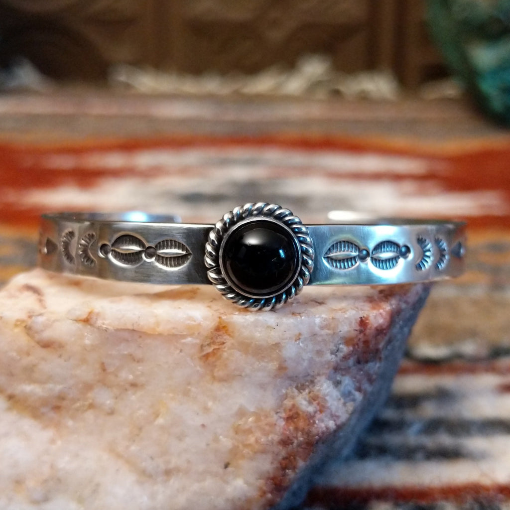 Sterling silver cuff with stamped designs on the band and black onyx set in a twisted rope bezel.