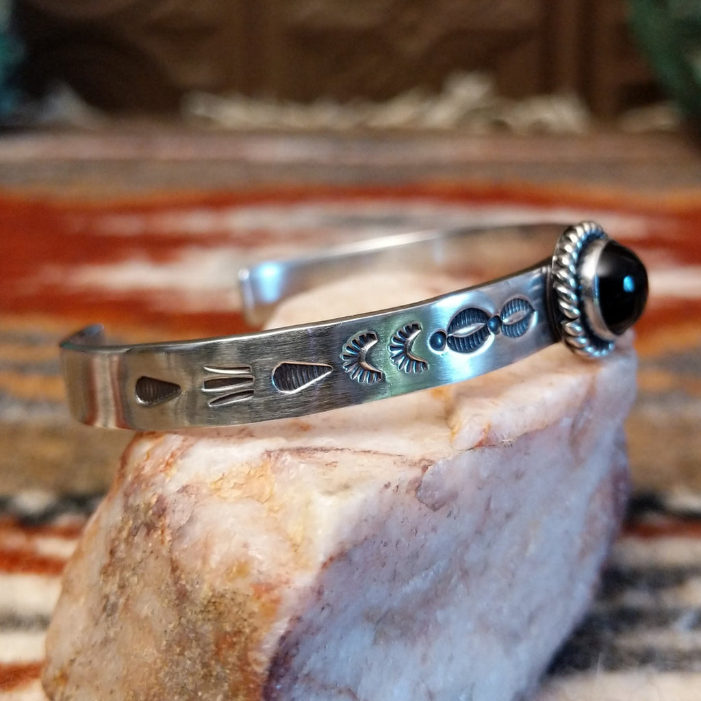 Sterling silver cuff with stamped designs on the band and black onyx set in a twisted rope bezel.
