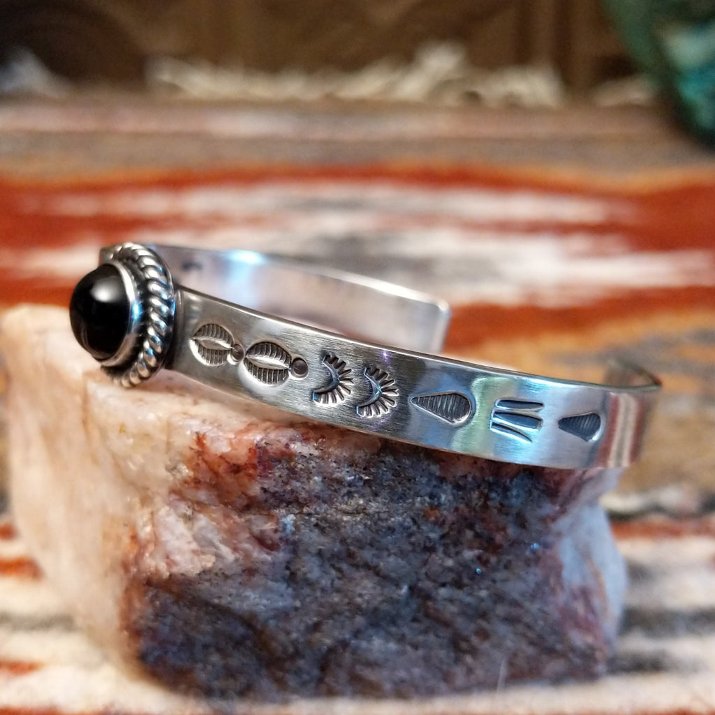 Sterling silver cuff with stamped designs on the band and black onyx set in a twisted rope bezel.