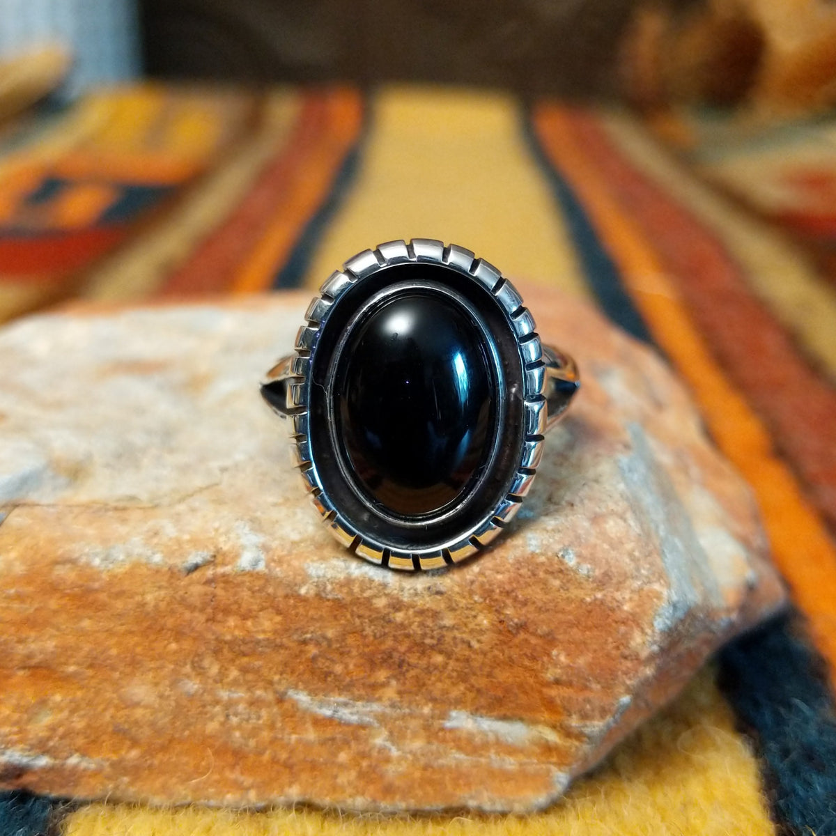 Front view of a silver ring featuring a glossy oval black onyx stone framed by a darkened silver recess and a raised, segmented silver border.