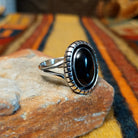 Angled view of a silver ring featuring an oval black onyx cabochon surrounded by a darkened recessed border, segmented silver detailing, and a polished split-shank band.