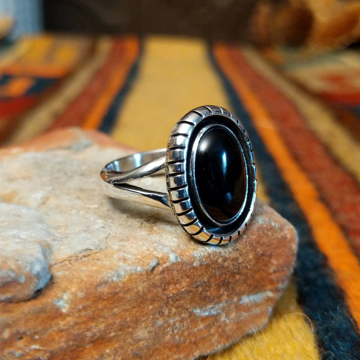 Angled view of a silver ring featuring an oval black onyx cabochon surrounded by a darkened recessed border, segmented silver detailing, and a polished split-shank band.