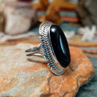 Sterling silver ring by Larson Lee featuring a large elongated oval black onyx cabochon framed by twisted silver rope and geometric silver detailing; side view.