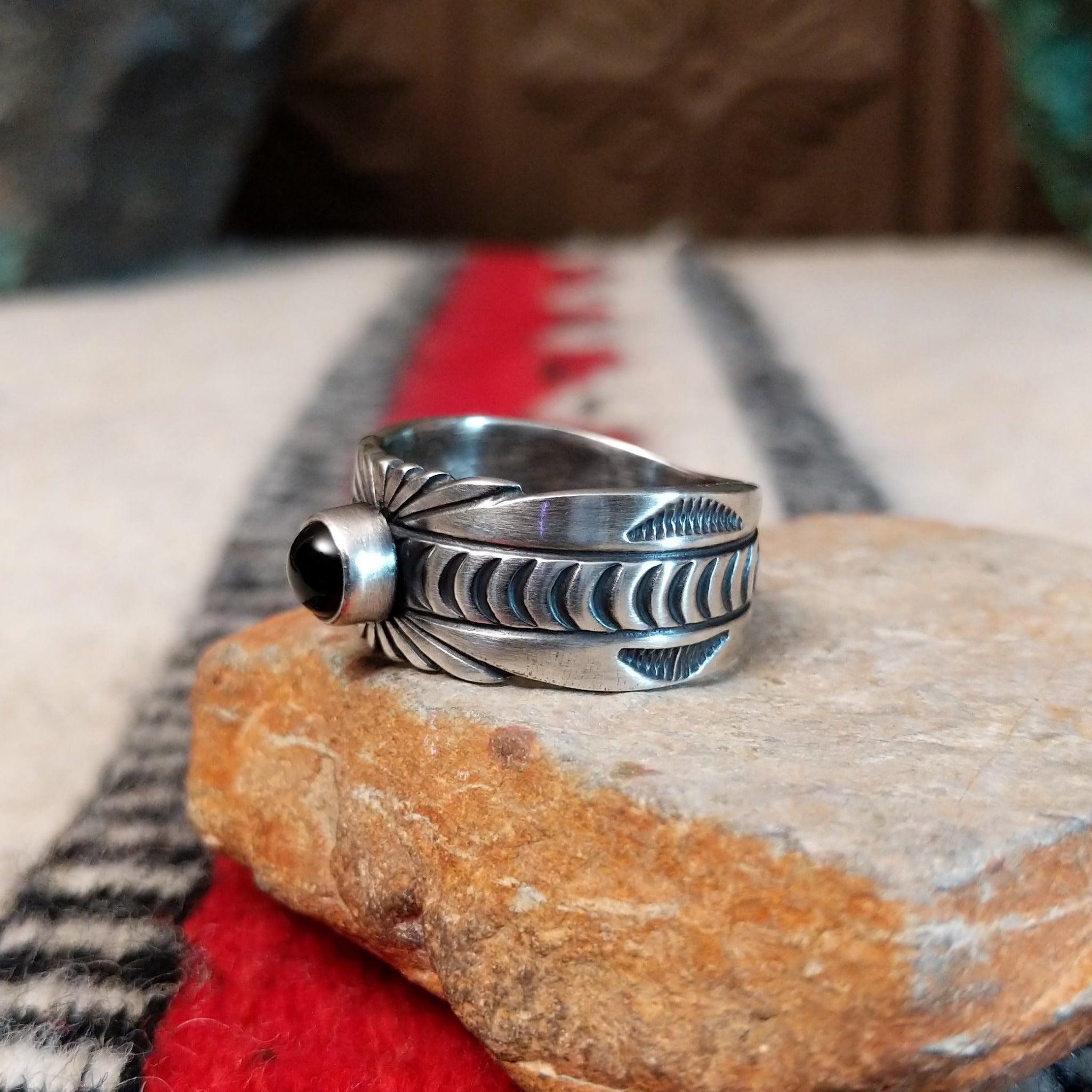 Black Onyx ring by Raymond Coriz featuring a round polished black stone centered in a wide silver band with detailed stamped, radiating, and curved designs; side view.