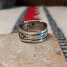 Black Onyx ring by Raymond Coriz featuring a round polished black stone centered in a wide silver band with detailed stamped, radiating, and curved designs; underside view.