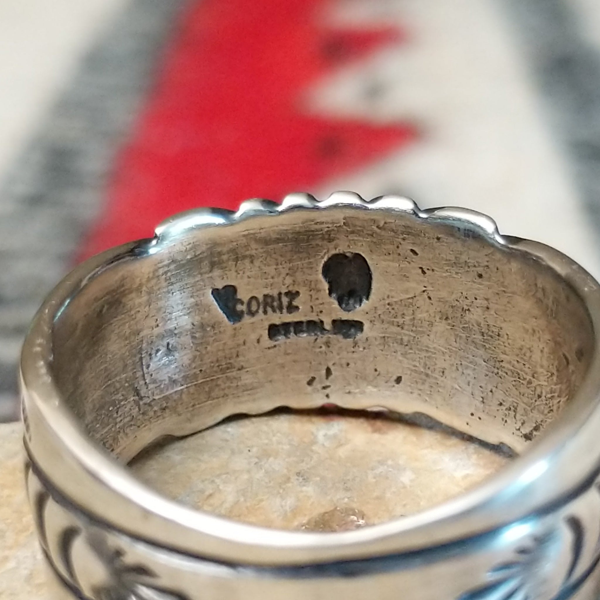 Black Onyx ring by Raymond Coriz featuring a round polished black stone centered in a wide silver band with detailed stamped, radiating, and curved designs; artisan and Sterling Silver stamp.