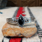 Silver cuff by Raymond Coriz featuring a polished teardrop-shaped black onyx surrounded by twisted wire, silver drops, stamped accents, and layered silver bands.