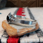 Silver cuff by Raymond Coriz featuring a polished teardrop-shaped black onyx surrounded by twisted wire, silver drops, stamped accents, and layered silver bands; side view.