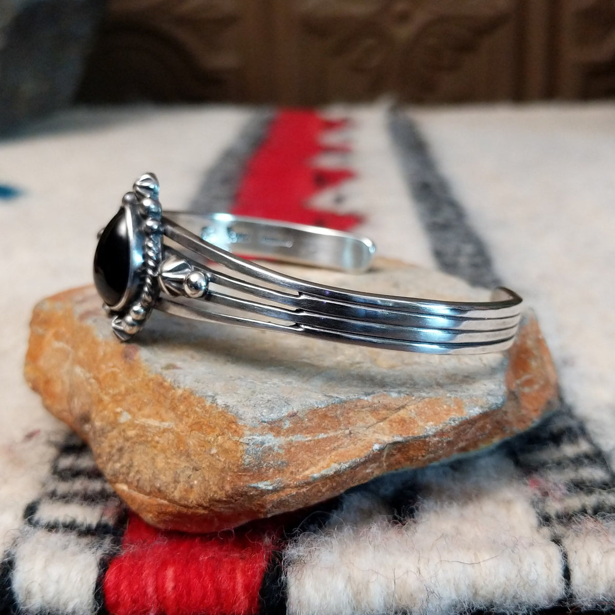 Silver cuff by Raymond Coriz featuring a polished teardrop-shaped black onyx surrounded by twisted wire, silver drops, stamped accents, and layered silver bands; side view.