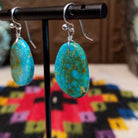 Blue-Green Turquoise Slab Earrings by Ronald Chavez featuring freeform blue-green turquoise stones with natural golden-brown matrix, suspended from silver hooks; side view.